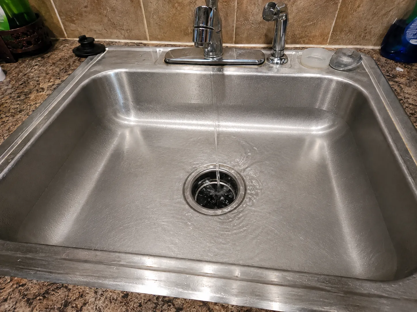 The same kitchen sink after clearing — empty, with water running freely down the open drain